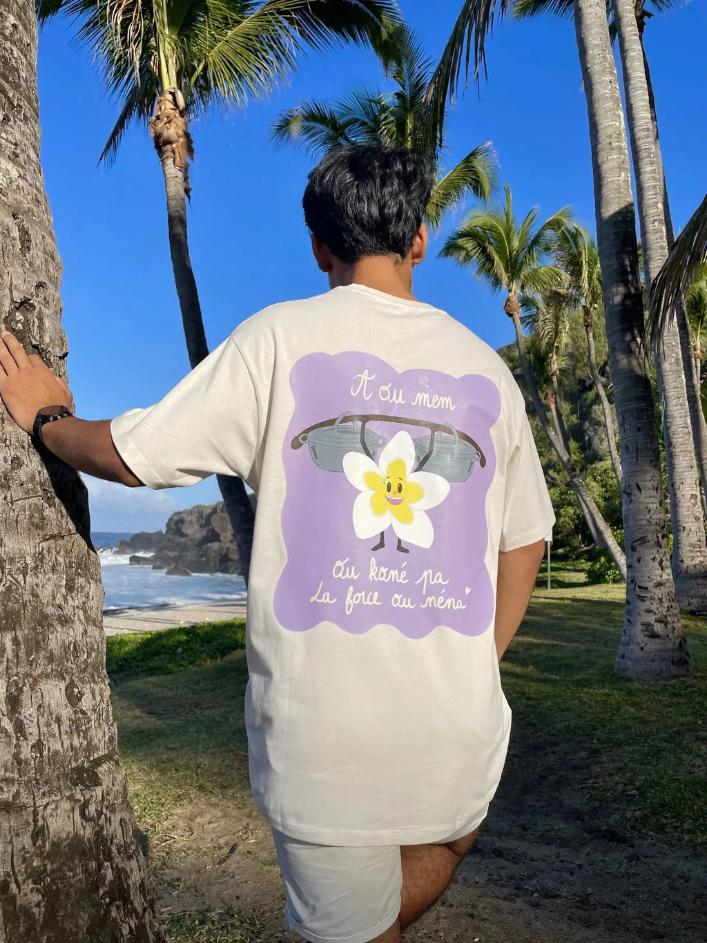 Man wearing graphic t-shirt with flower design by palm trees on a tropical beach